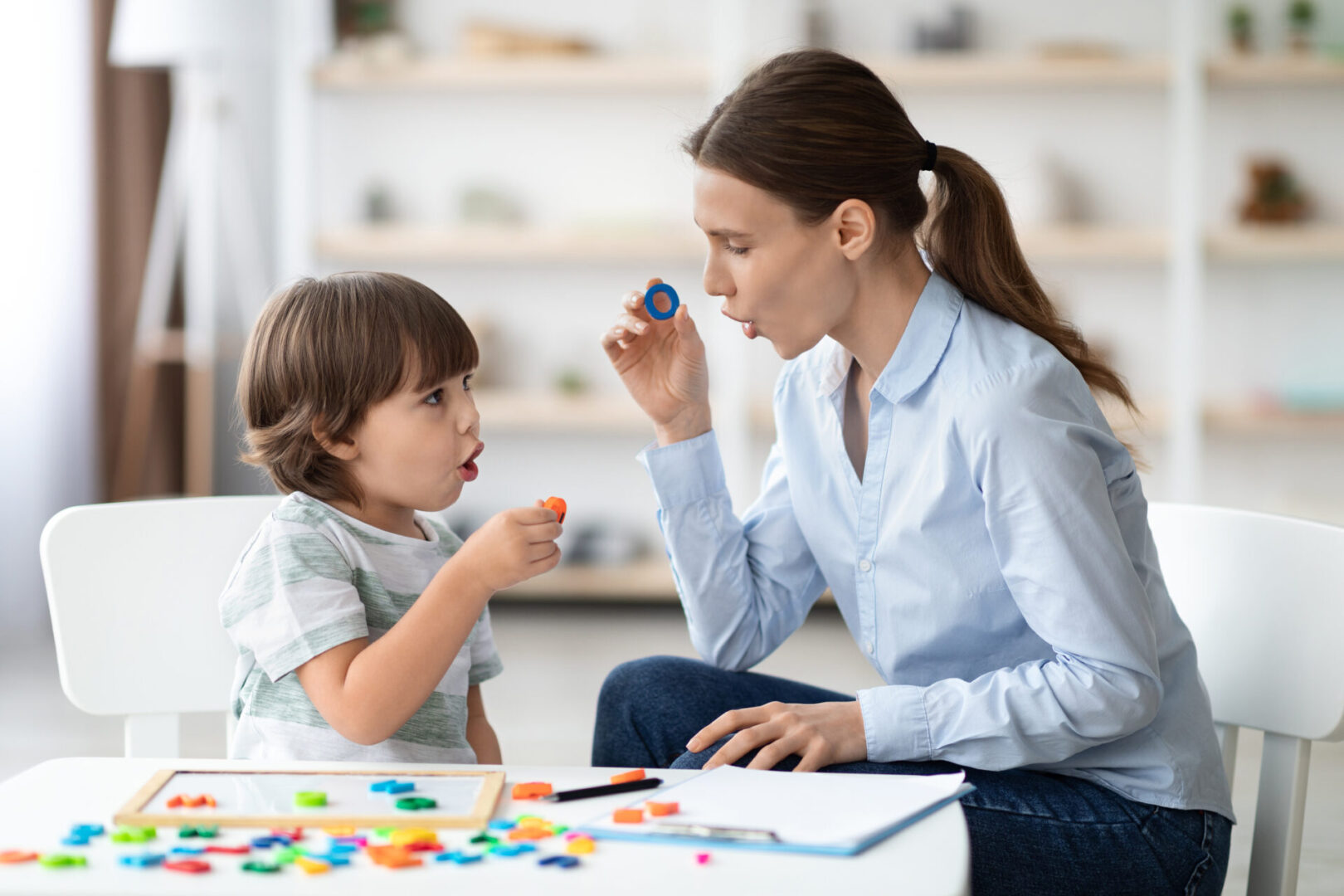 Female speech therapist curing child's problems and impediments. Little boy learning letter O with private tutor A woman and child are playing with colorful blocks.