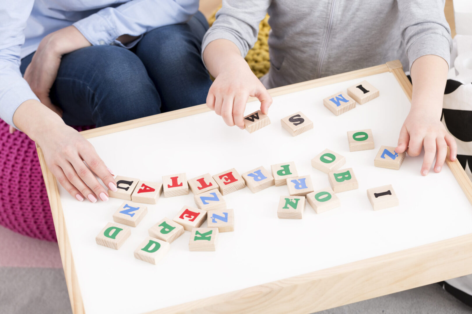 Woman and girl playing with building blocks Two people sitting at a white table arranging alphabet blocks.